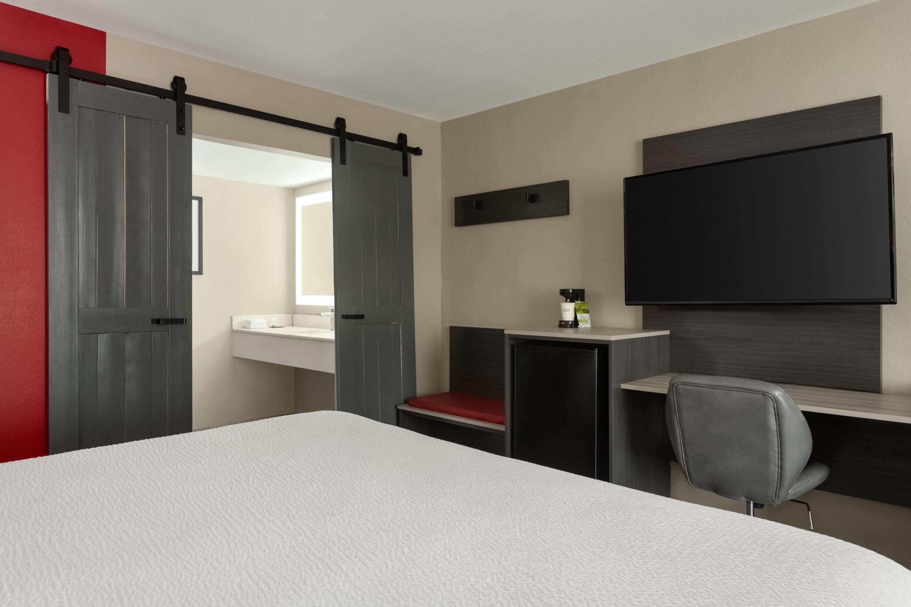 Habitació d'hotel amb un llit, un escriptori, una cadira, un televisor i una porta corredissa.