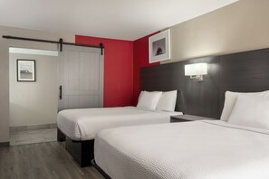 Habitación de hotel con dos camas, un armario, un cuadro en la pared y una mesita de noche con lámpara.