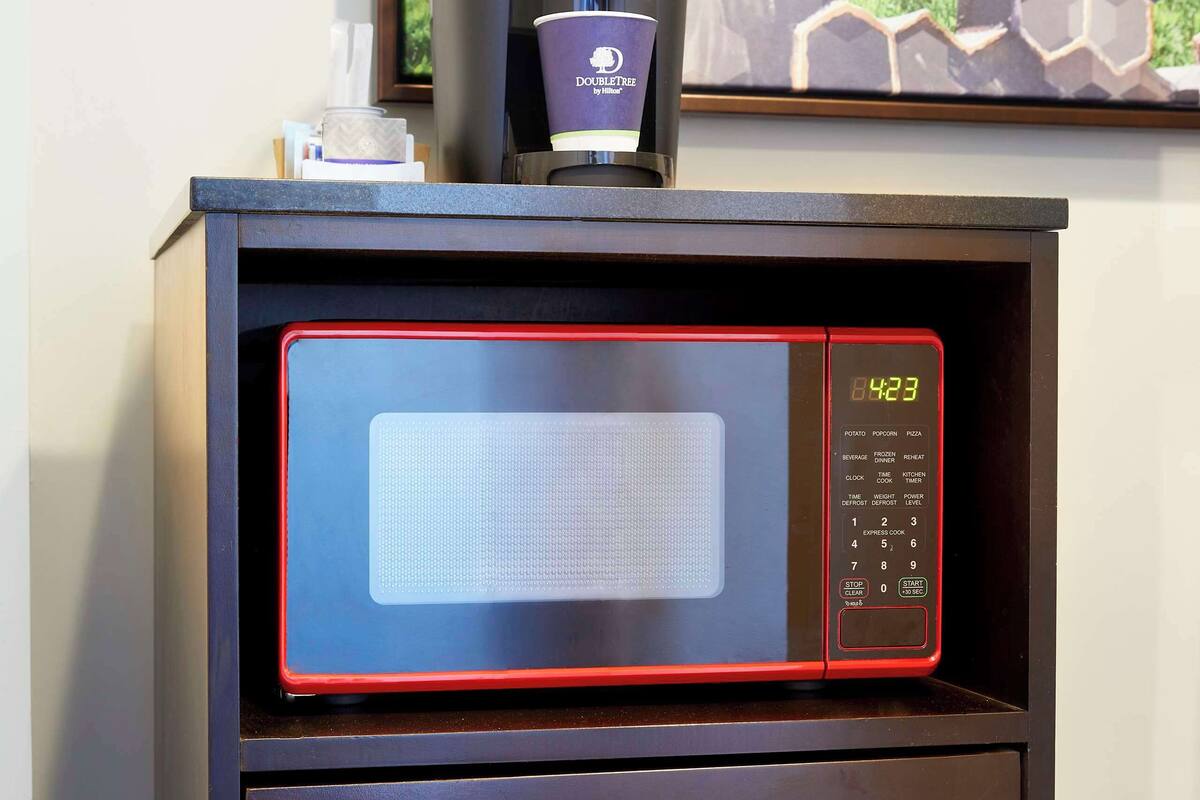 A microwave with a digital display and a coffee maker on top.