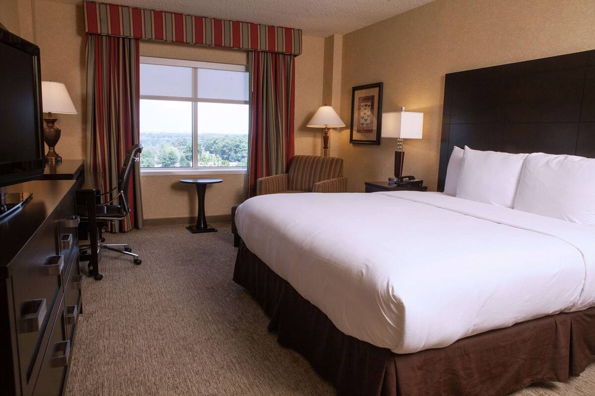 A hotel room with a large bed, a desk with a chair, a small table, and a TV.