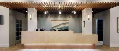 Un hall d’hôtel avec un plafond en bois, un comptoir d’accueil et un grand tableau abstrait accroché au mur.
