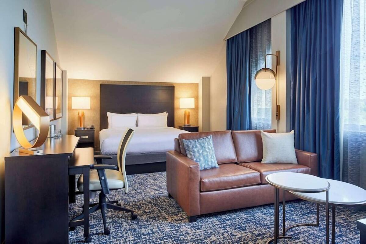 A hotel room with a bed, a sofa, a desk, and a lamp.
