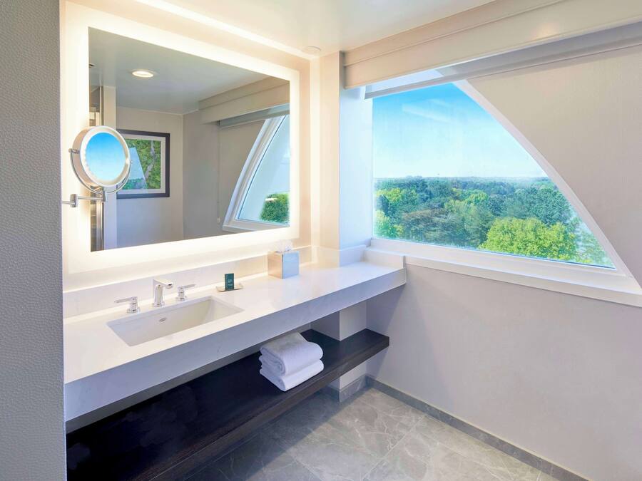 Uma casa de banho moderna com um espelho grande, uma pia e uma janela com vista para uma floresta.