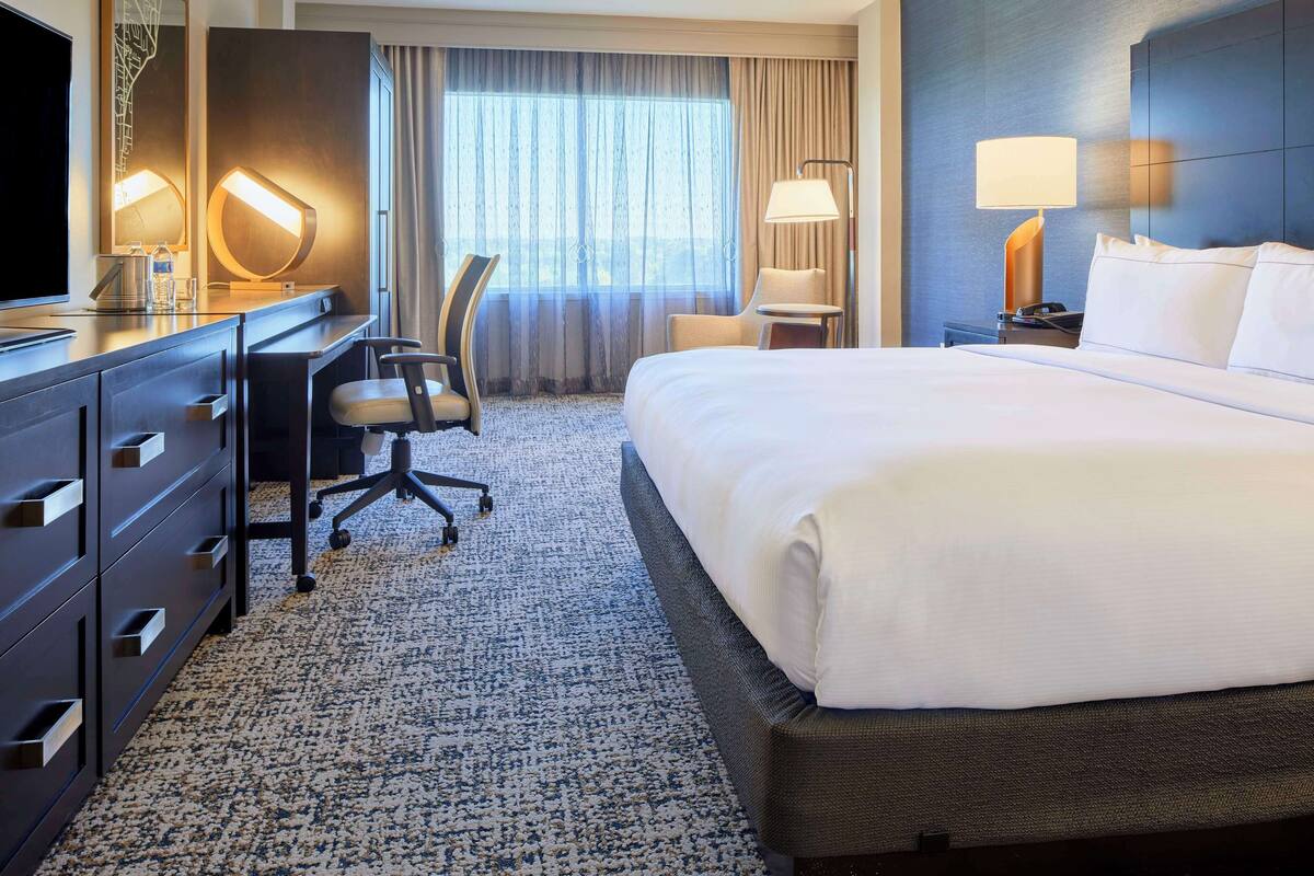 A hotel room with a large bed, a desk with a chair, a television, and a lamp.