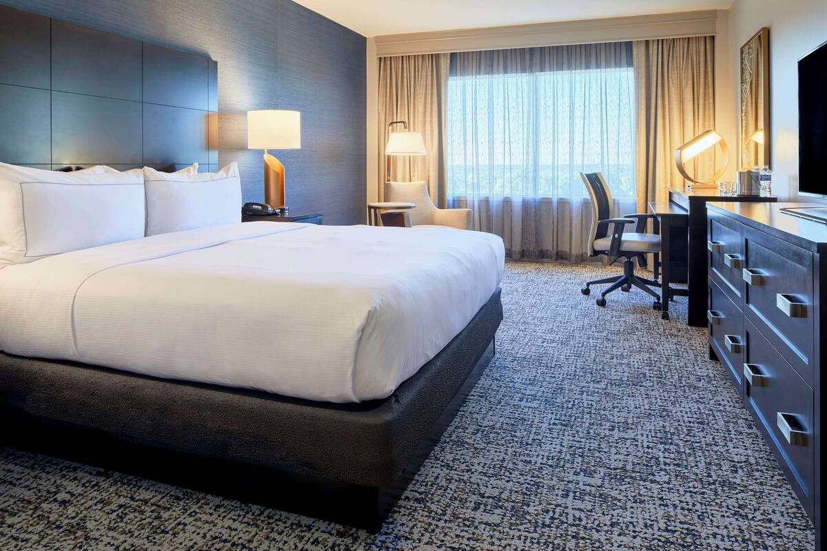 A hotel room with a large bed, a desk with a chair, a dresser, and a television.