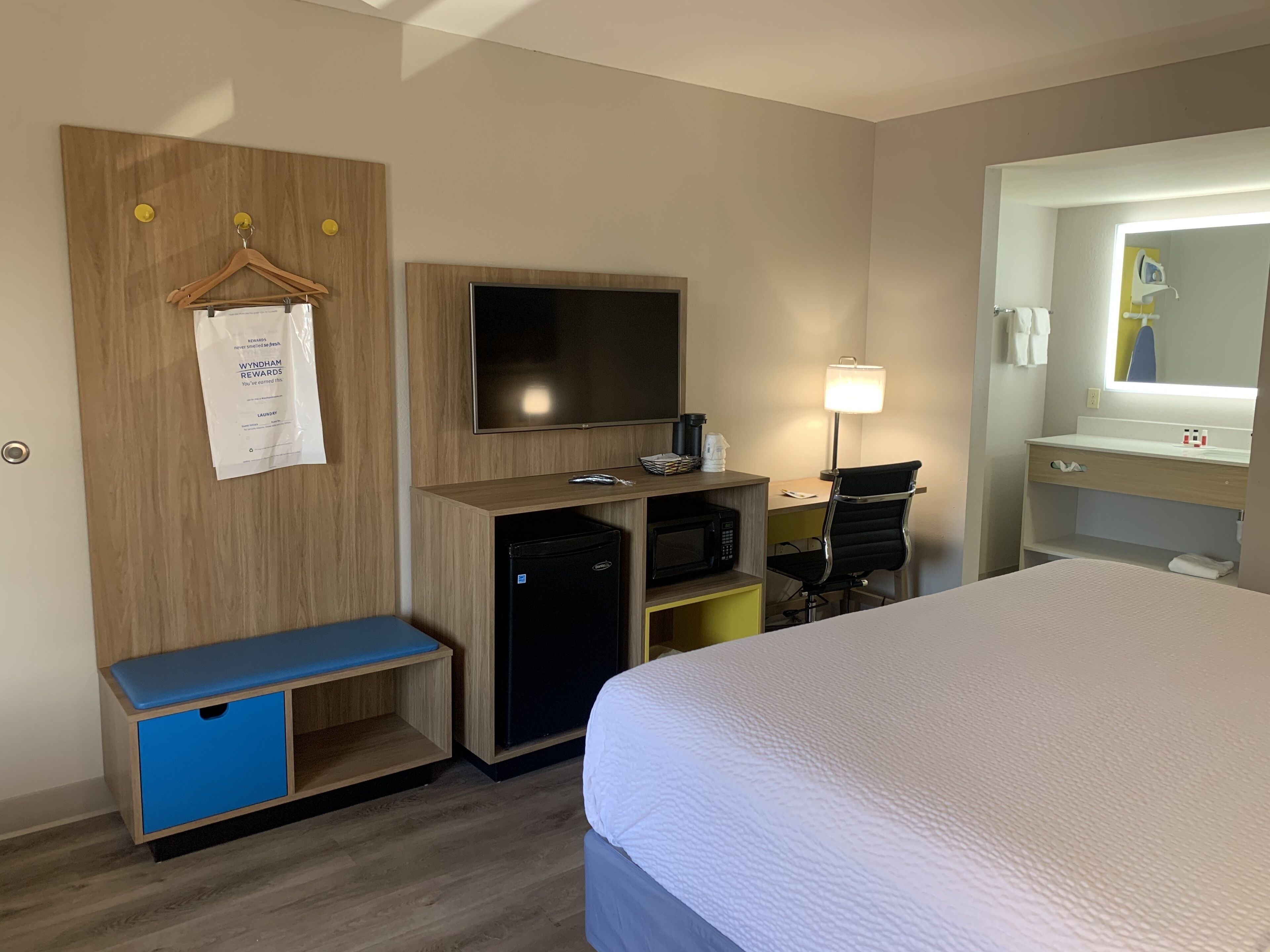 A hotel room with a bed, a desk with a computer, a TV, a microwave, and a small seating area.