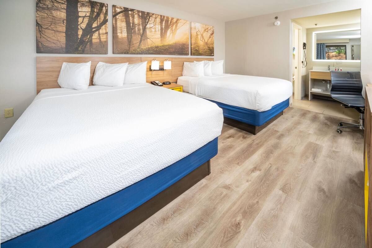 Habitación de hotel con dos camas, cabecero de madera, un ventanal grande y un escritorio con una silla.