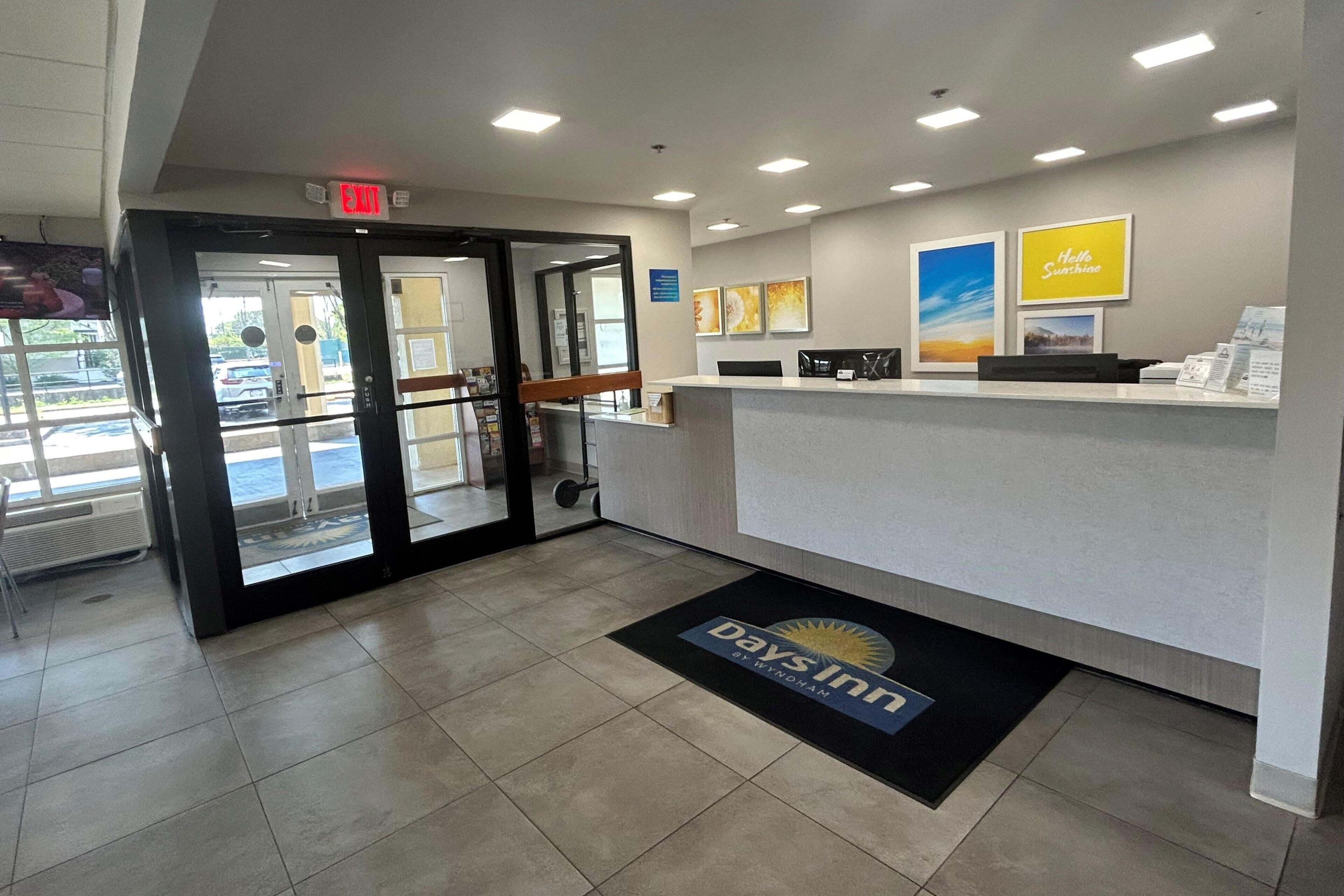 A reception area with a glass door entrance, a reception desk, and a doormat with the Days Inn logo.