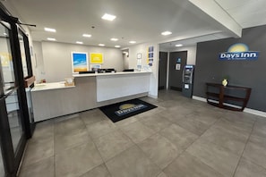 Un área de recepción con mostrador, un cartel de Days Inn y una pequeña planta sobre una mesa.