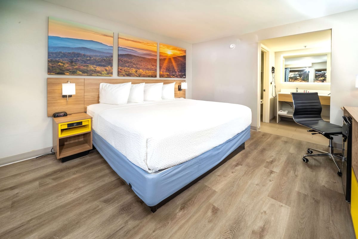 Una habitación de hotel con una cama grande, un escritorio con silla, una lámpara de escritorio y un espejo.