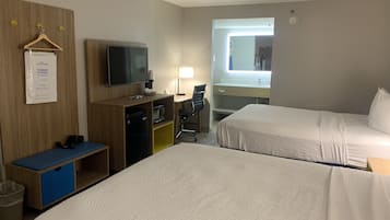 Habitación de hotel con dos camas, un escritorio con computadora, televisor y una kitchenette pequeña.