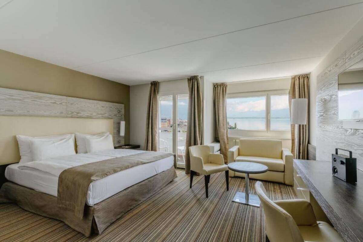 Habitación de hotel con cama, sofá, una mesita, televisión y vistas a la ciudad.