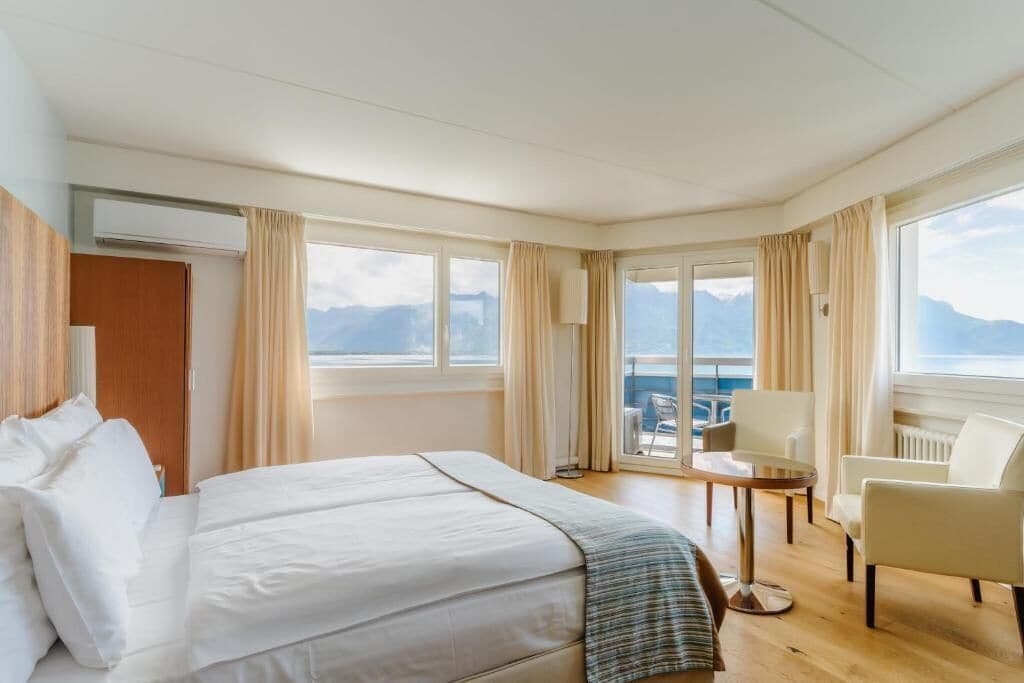 A hotel room with a bed, a chair, a table, and a view of the sea.