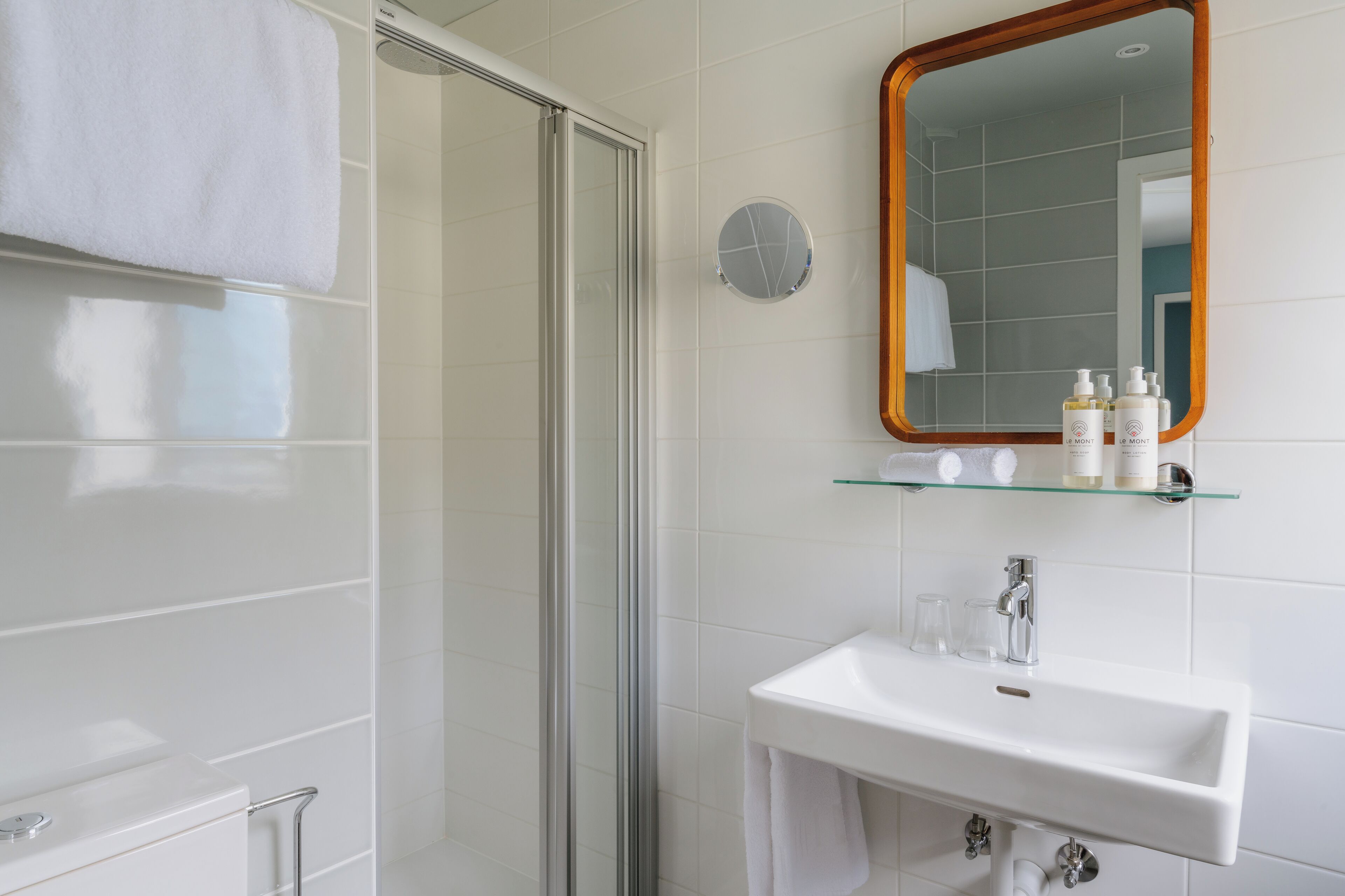 A modern bathroom with a glass shower enclosure, a white sink with a mirror above it, and toiletries on a glass shelf.