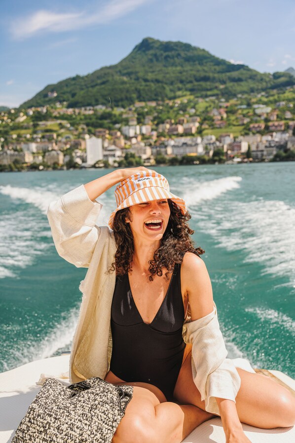 A person sitting on a boat with a mountainous landscape in the background. - Mona Montreux (Montreux)