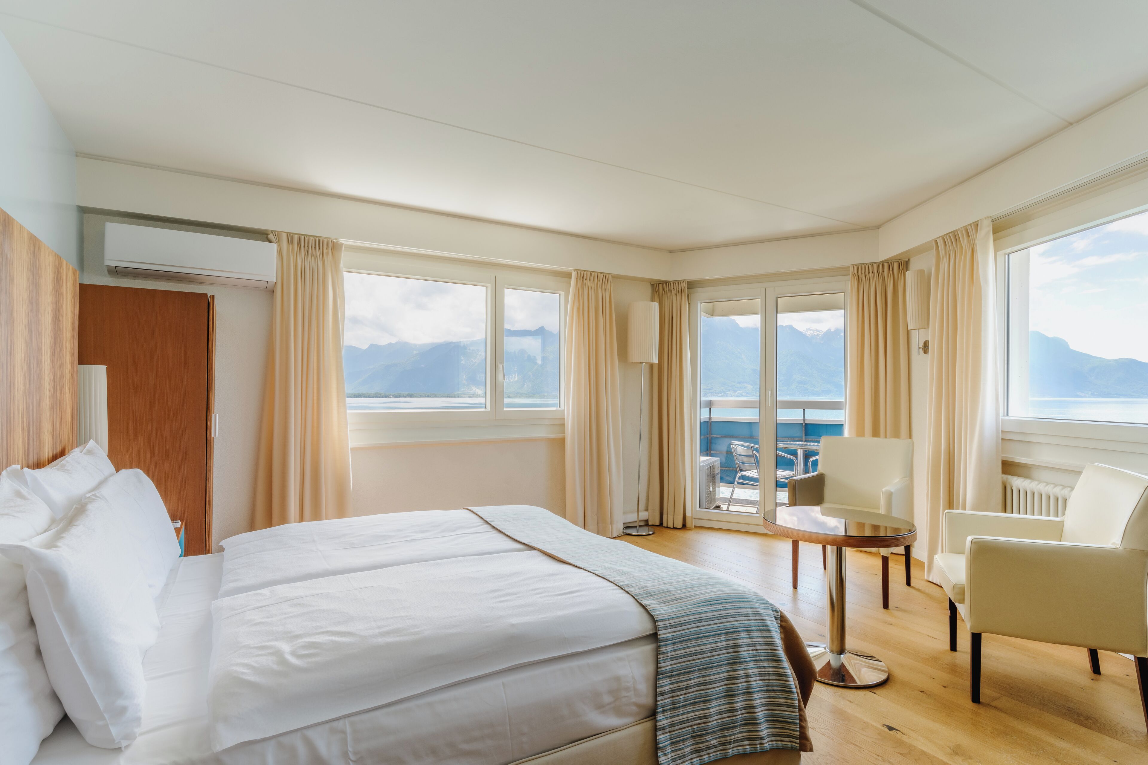 Hotelkamer met een groot bed, een klein tafeltje, een stoel en uitzicht op de bergen door de ramen.