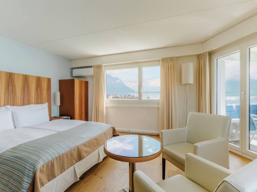Una habitación de hotel con cama, una mesita redonda, una silla y vistas al mar a través de amplios ventanales.