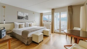 Hotelkamer met een bed, een tafel, een stoel, een bureau, een lamp, een schilderij aan de muur en uitzicht op zee.