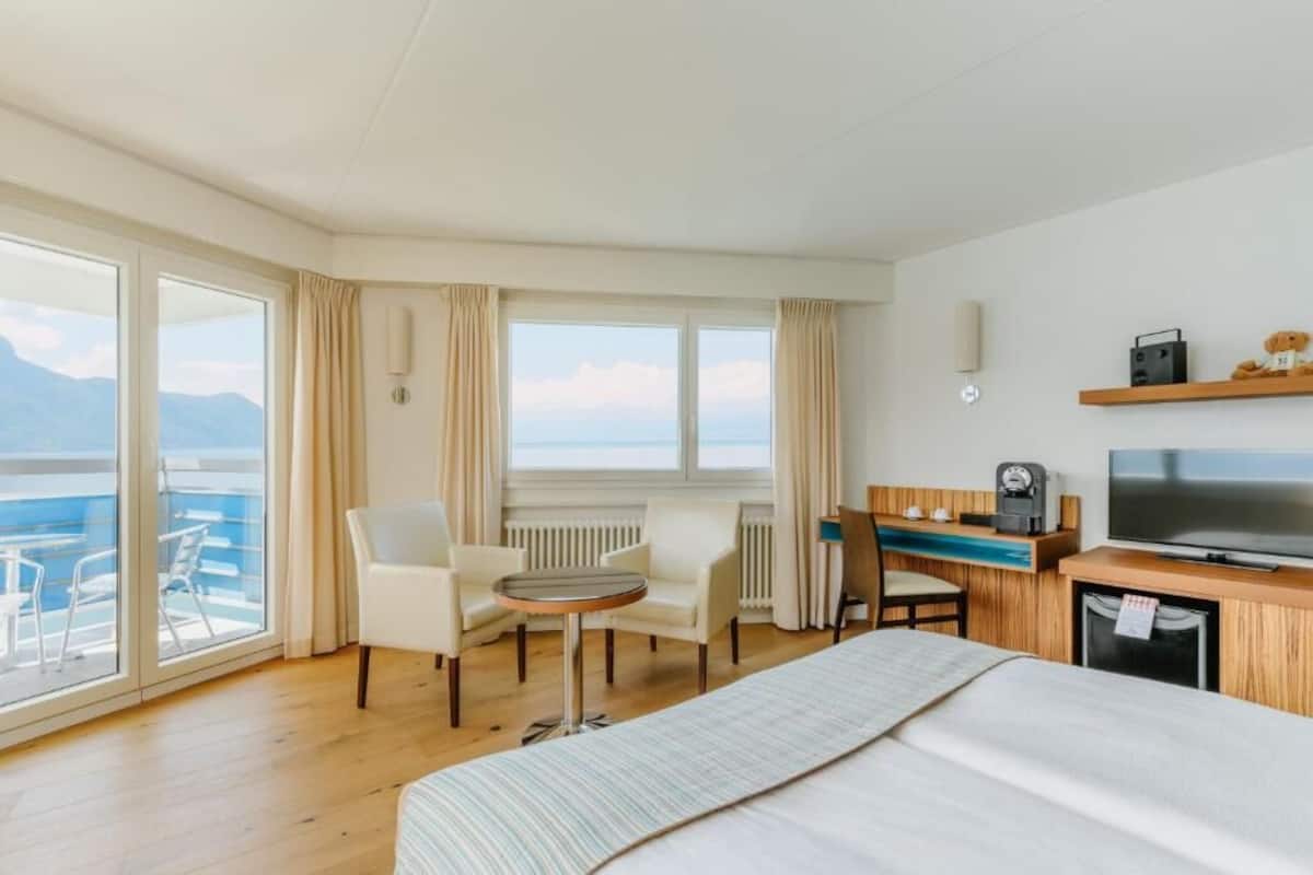 Habitación de hotel con cama, escritorio con televisor, una silla, una mesita y vista al mar.