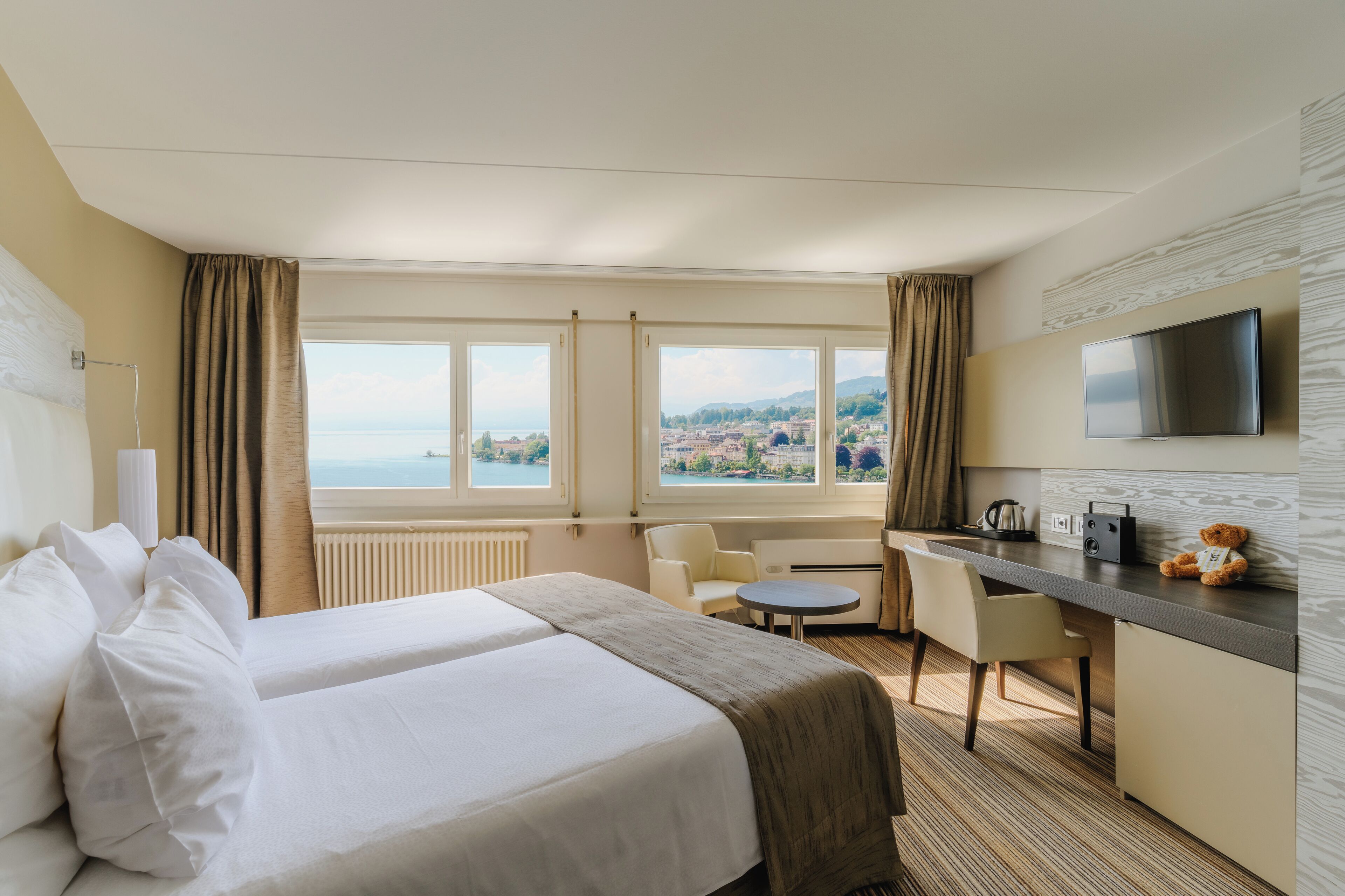 A hotel room with a bed, a desk, a chair, a television, and a view of the city.