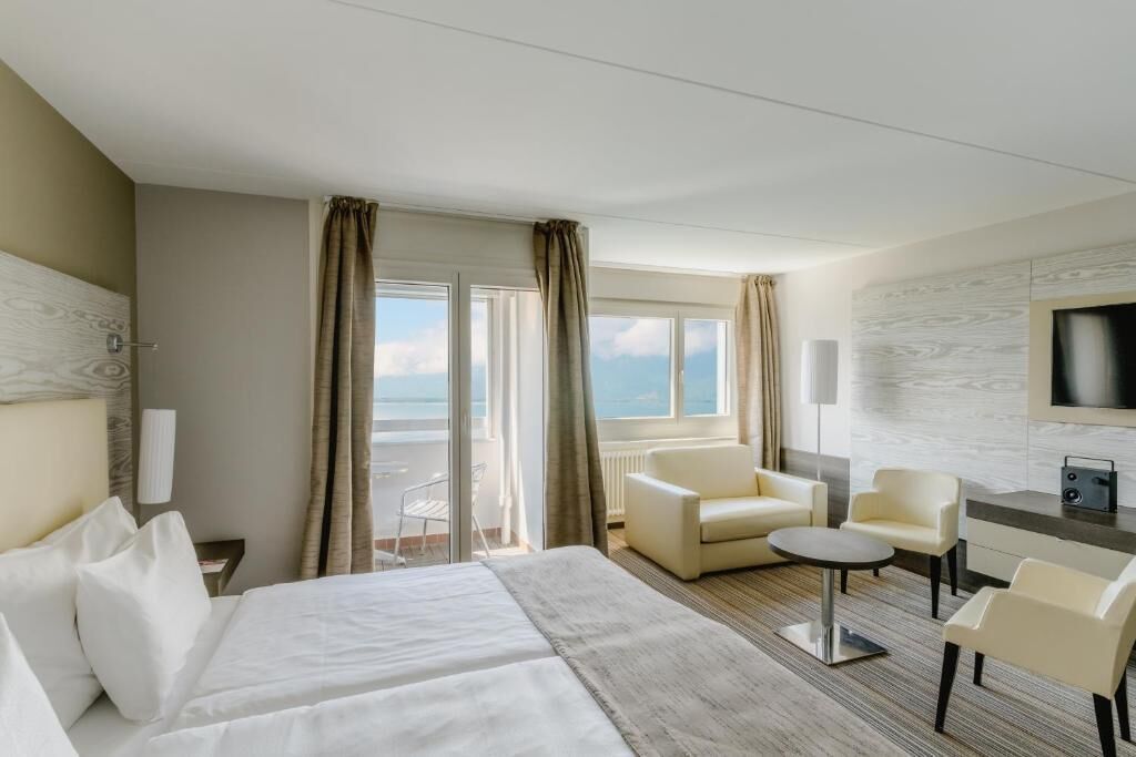 Una camera d'albergo con un letto, due poltrone, un tavolino, una TV e vista mare.