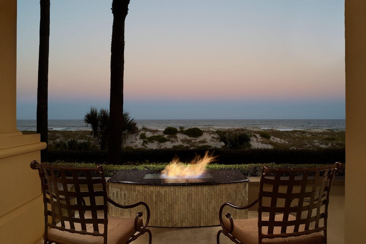 A patio with a fire feature, two chairs, and a view of the ocean.