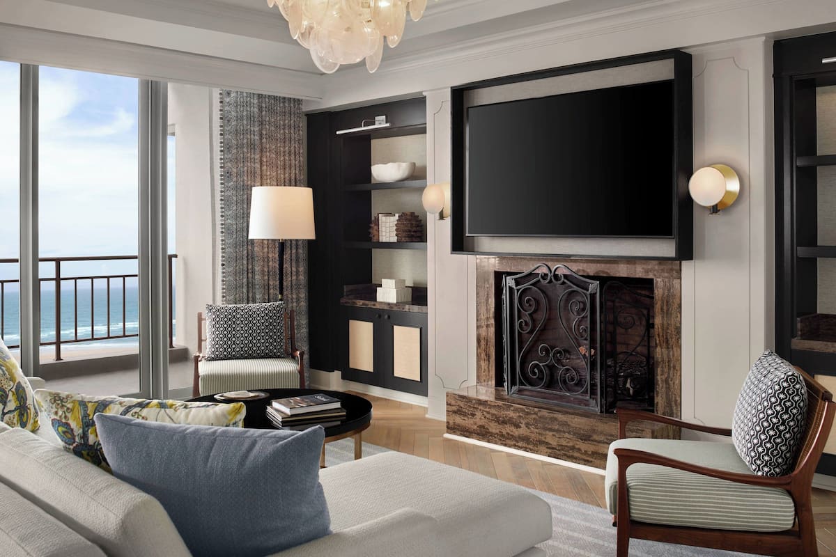 A modern living room with a fireplace, a large flat-screen TV, and a view of the ocean.