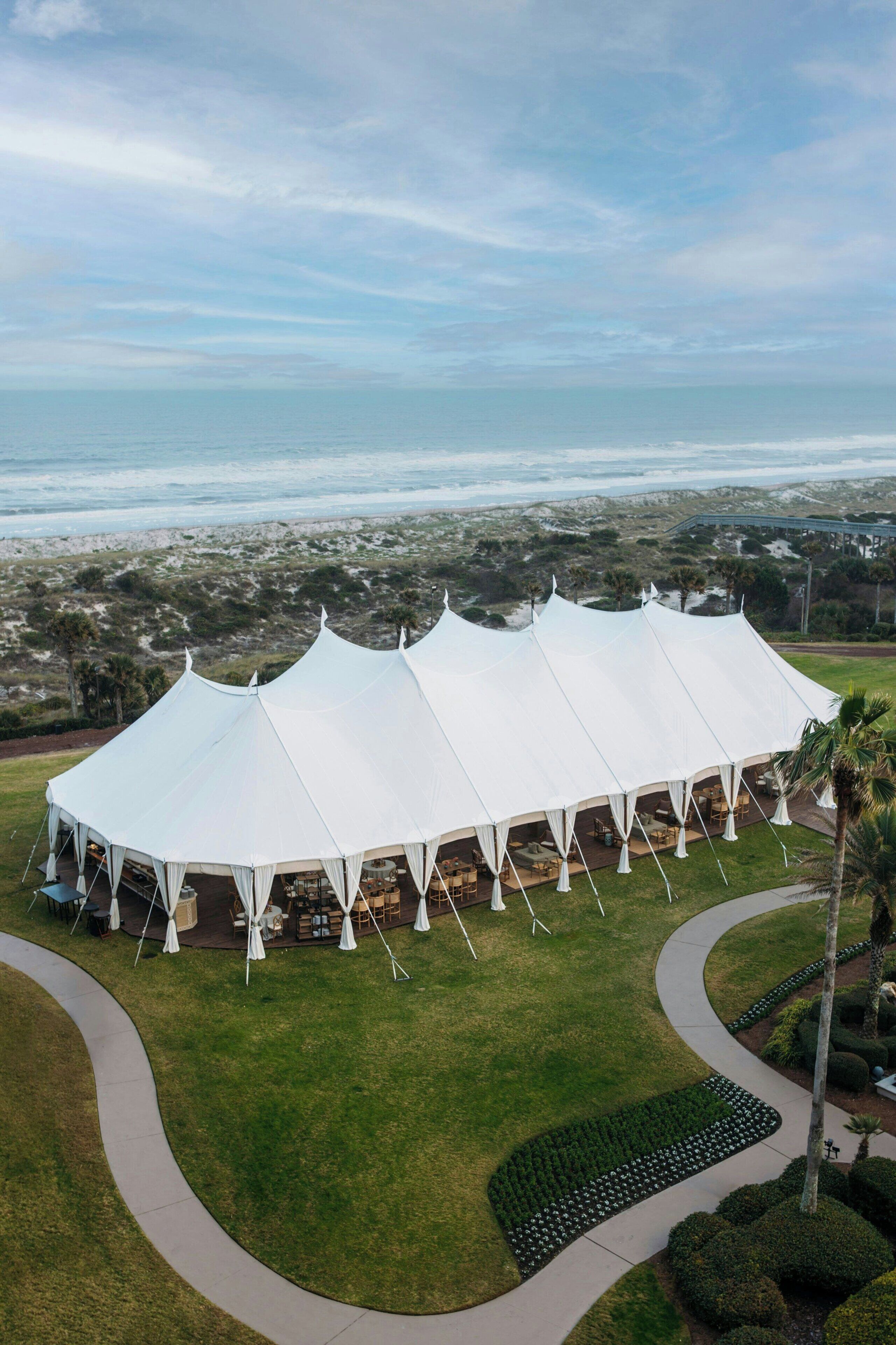 A large white tent structure with multiple seating areas, surrounded by a well-maintained lawn and a curved pathway.