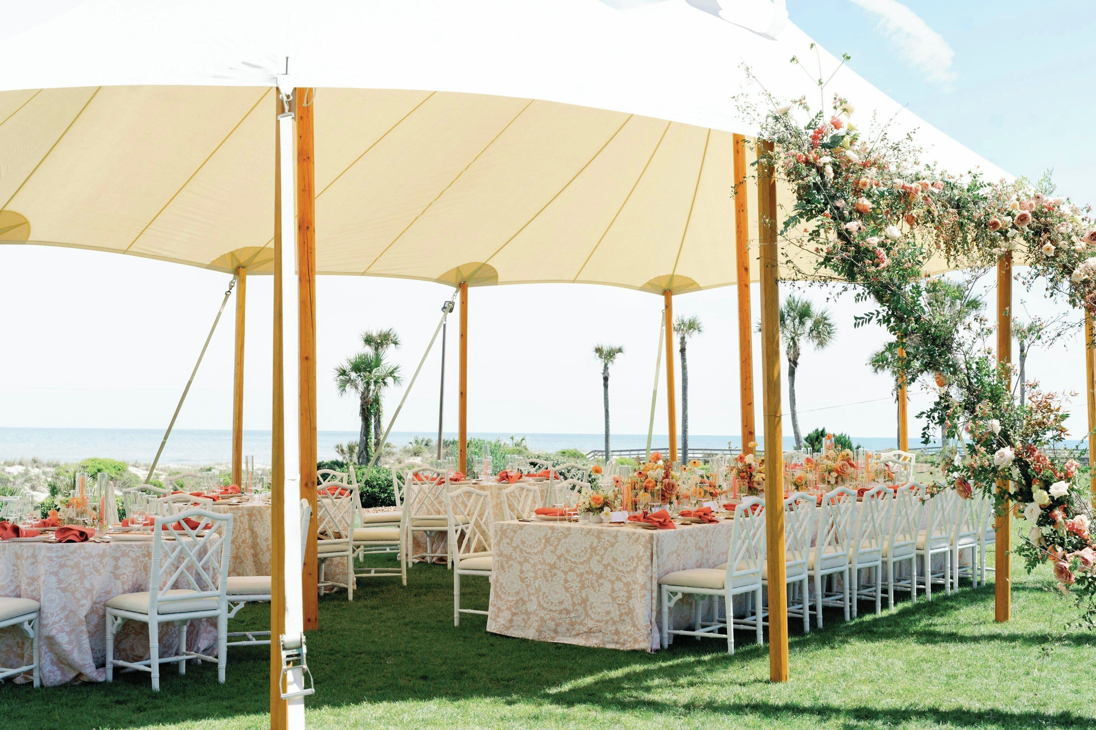 Un lieu de réception en plein air pour les mariages, avec des tables rondes, des chaises blanches et des décorations florales.