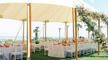 Um espaço para casamento ao ar livre com mesas redondas, cadeiras brancas e decorações florais.
