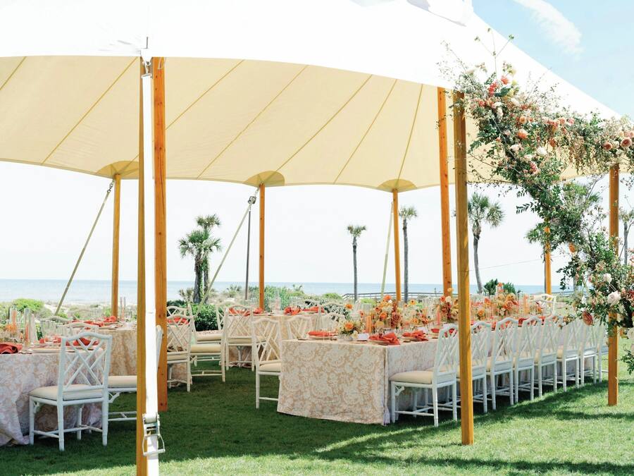 Um espaço para casamento ao ar livre com mesas redondas, cadeiras brancas e decorações florais.