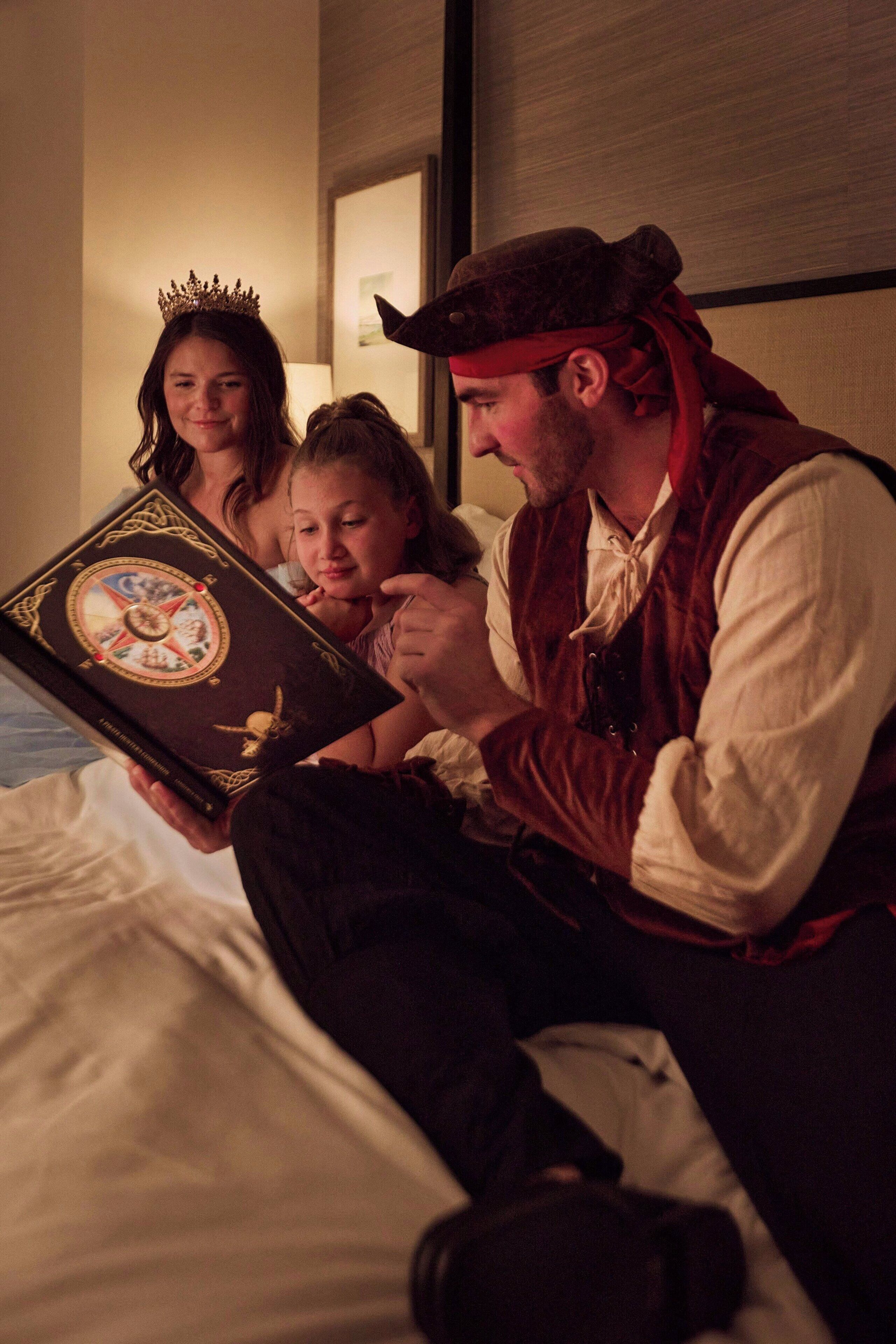 A person sitting on a bed with a book, another person leaning on the bed, and a third person partially visible.