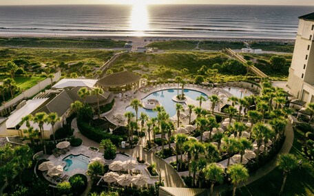 A resort with multiple swimming pools, palm trees, and a view of the ocean.
