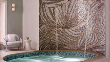Relax in a serene space with a hot tub and mosaic wall, accompanied by a wicker chair and a small side table.