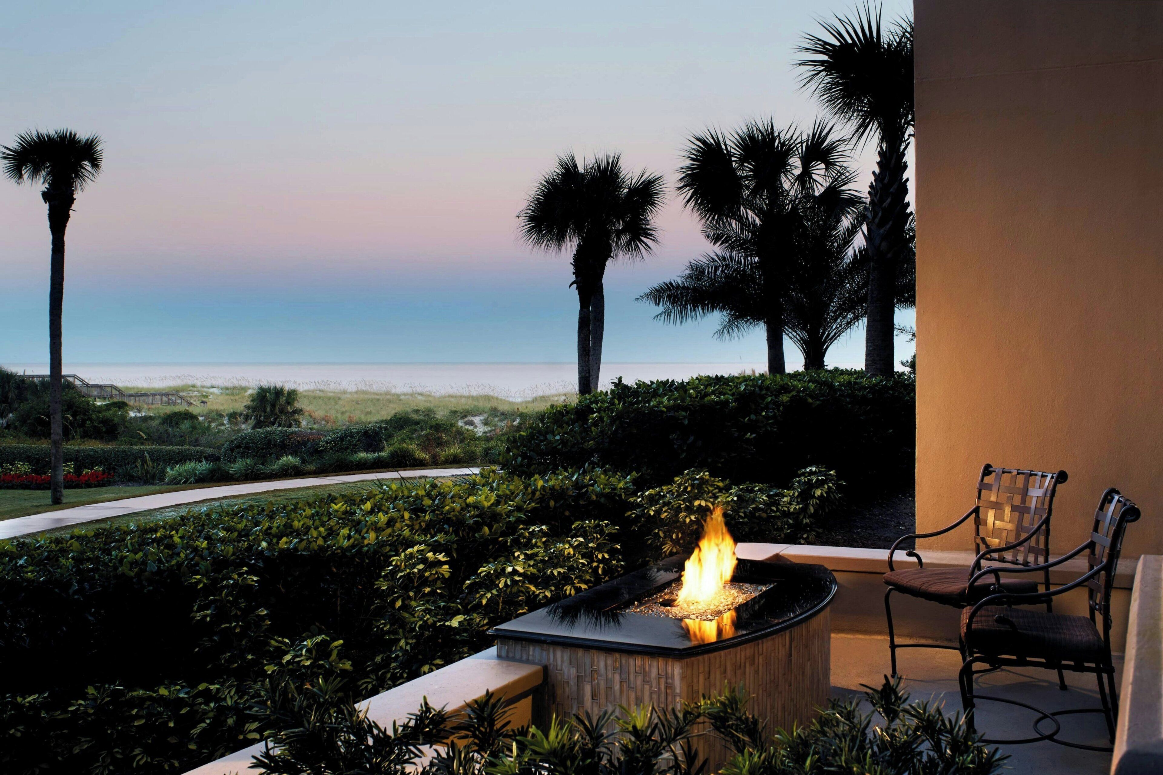 A patio with a fire feature, chairs, and a view of the ocean.