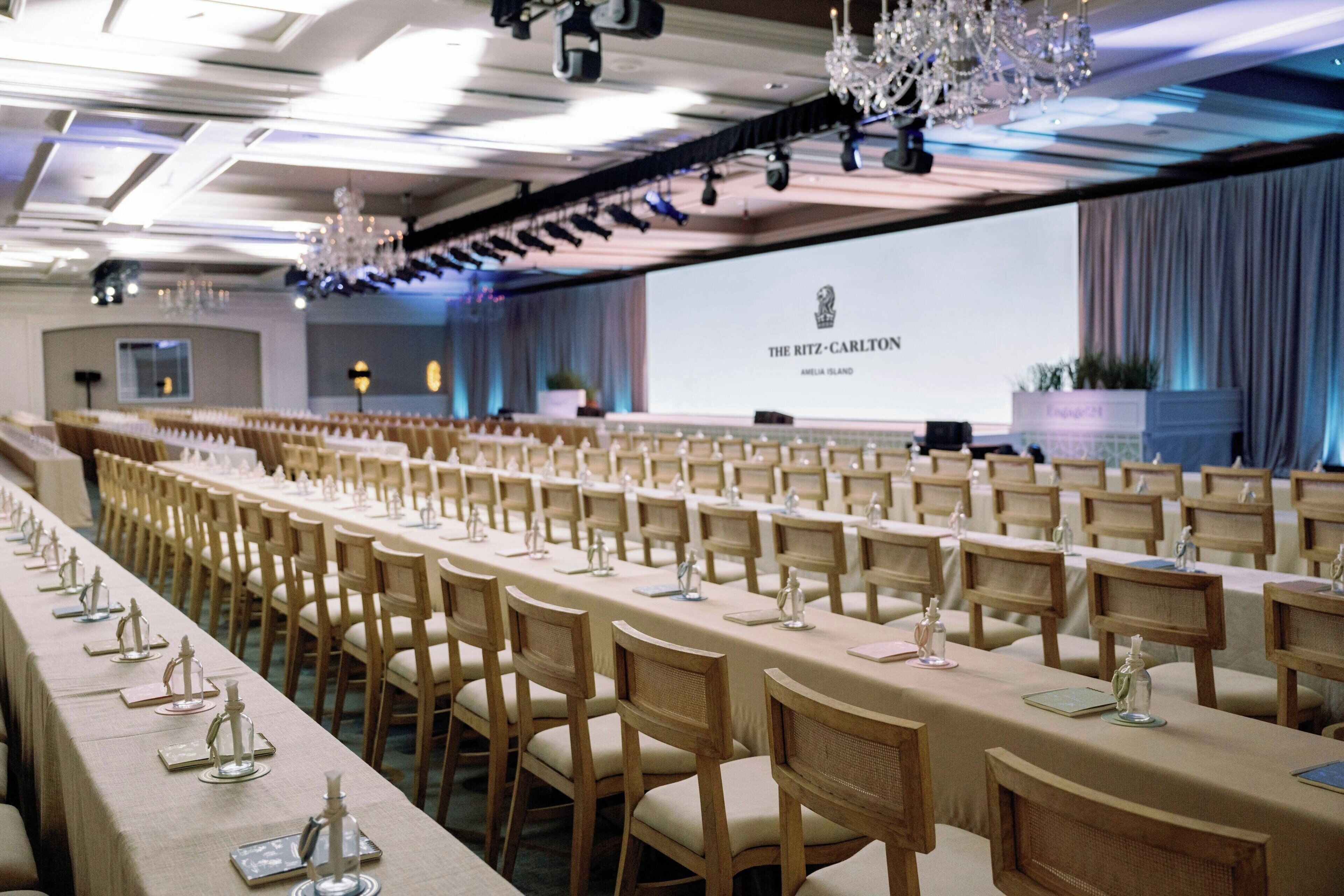 A conference room with long tables, wooden chairs, and a projection screen displaying "The Ritz-Carlton Amelia Island".