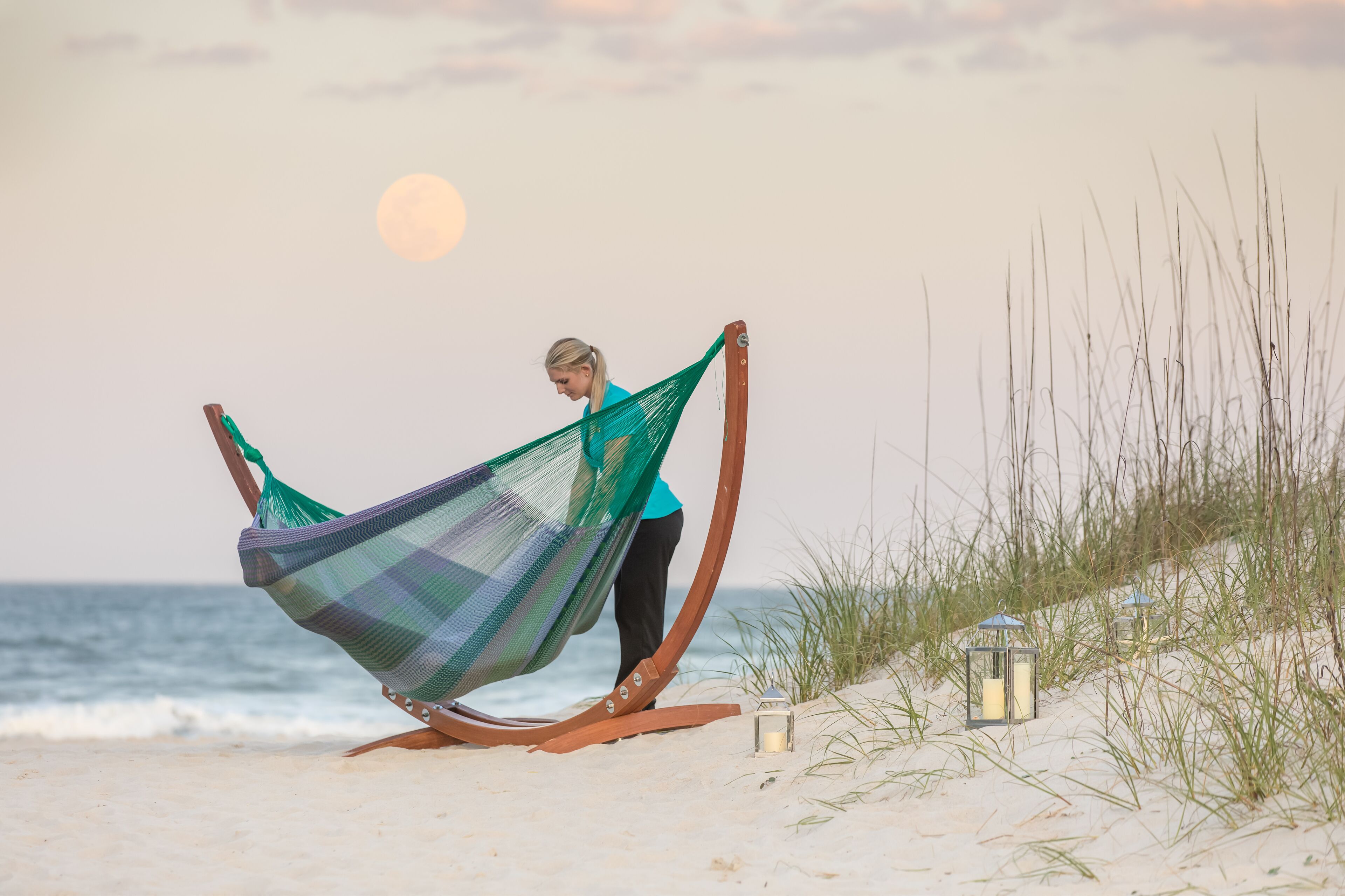 A hammock on a sandy beach with a lantern nearby.