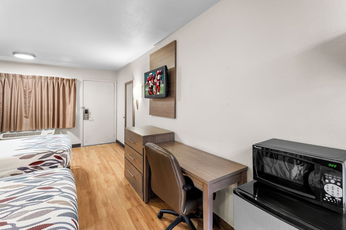 Ein Hotelzimmer mit Bett, Schreibtisch, Stuhl, Mikrowelle und Fernseher an der Wand.
