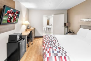 Een hotelkamer met een bed, een bureau met een lamp, een televisie, een koelkast en een badkamer zichtbaar door een geopende deur.