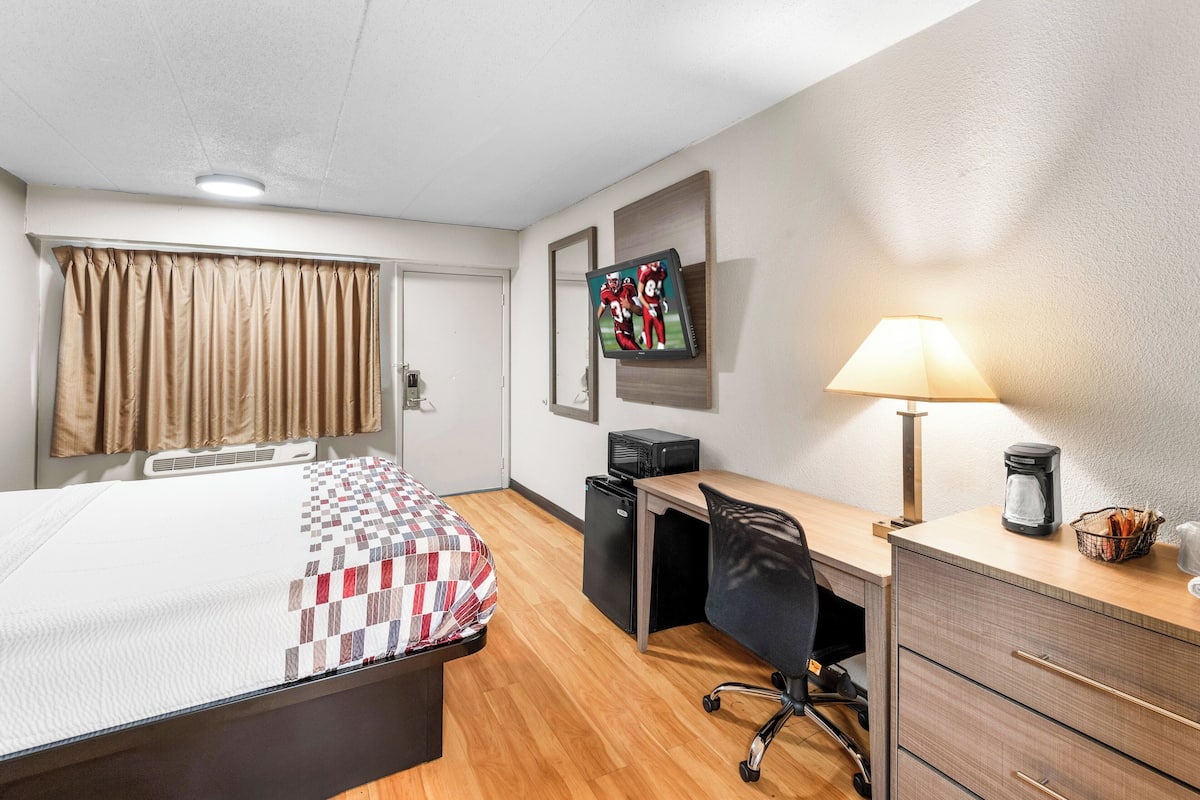 Ein Hotelzimmer mit Bett, Schreibtisch, Stuhl und einem Fernseher an der Wand.