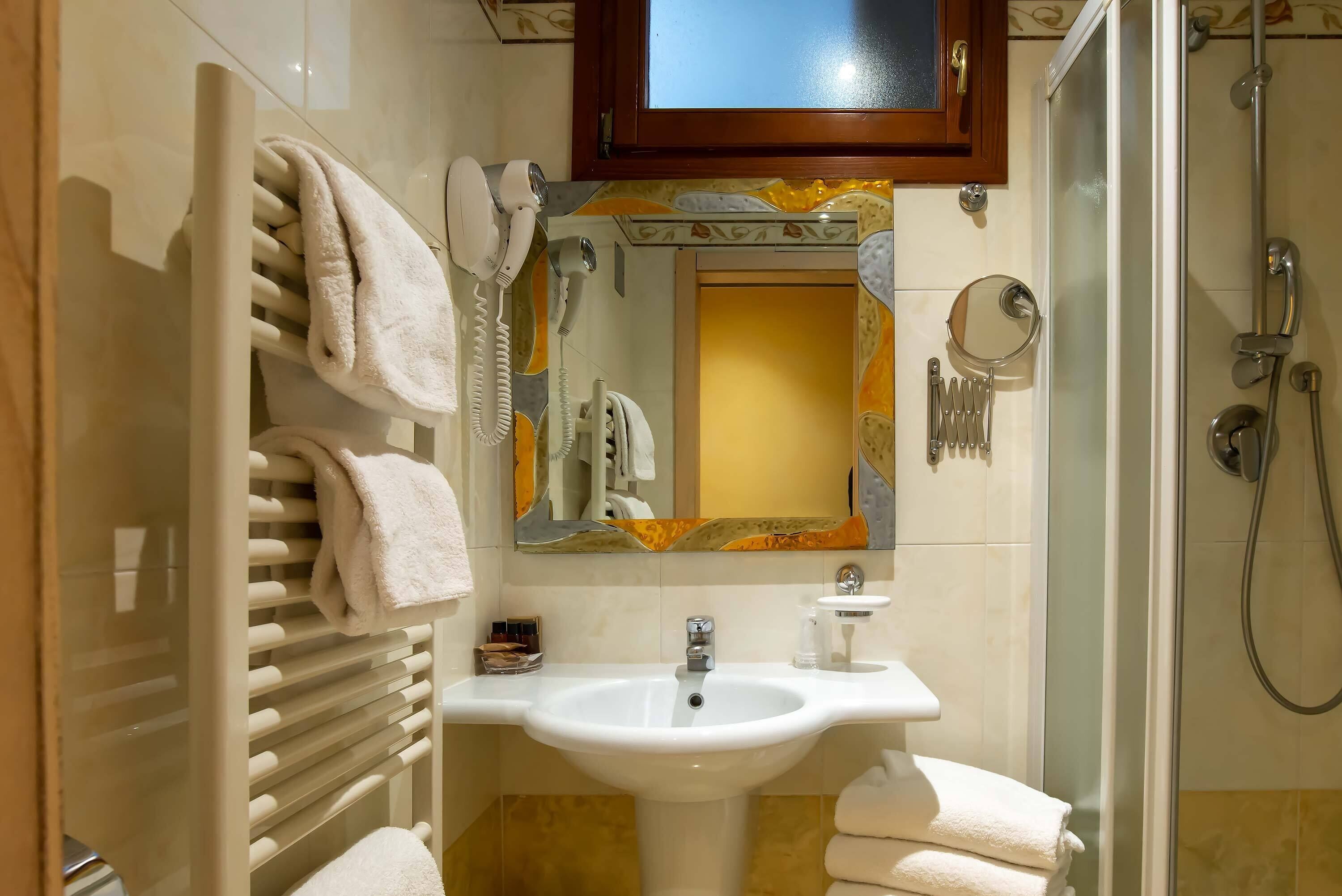 Un baño con un lavabo blanco, un perchero para toallas, un secador de pelo, un espejo y una zona de ducha.