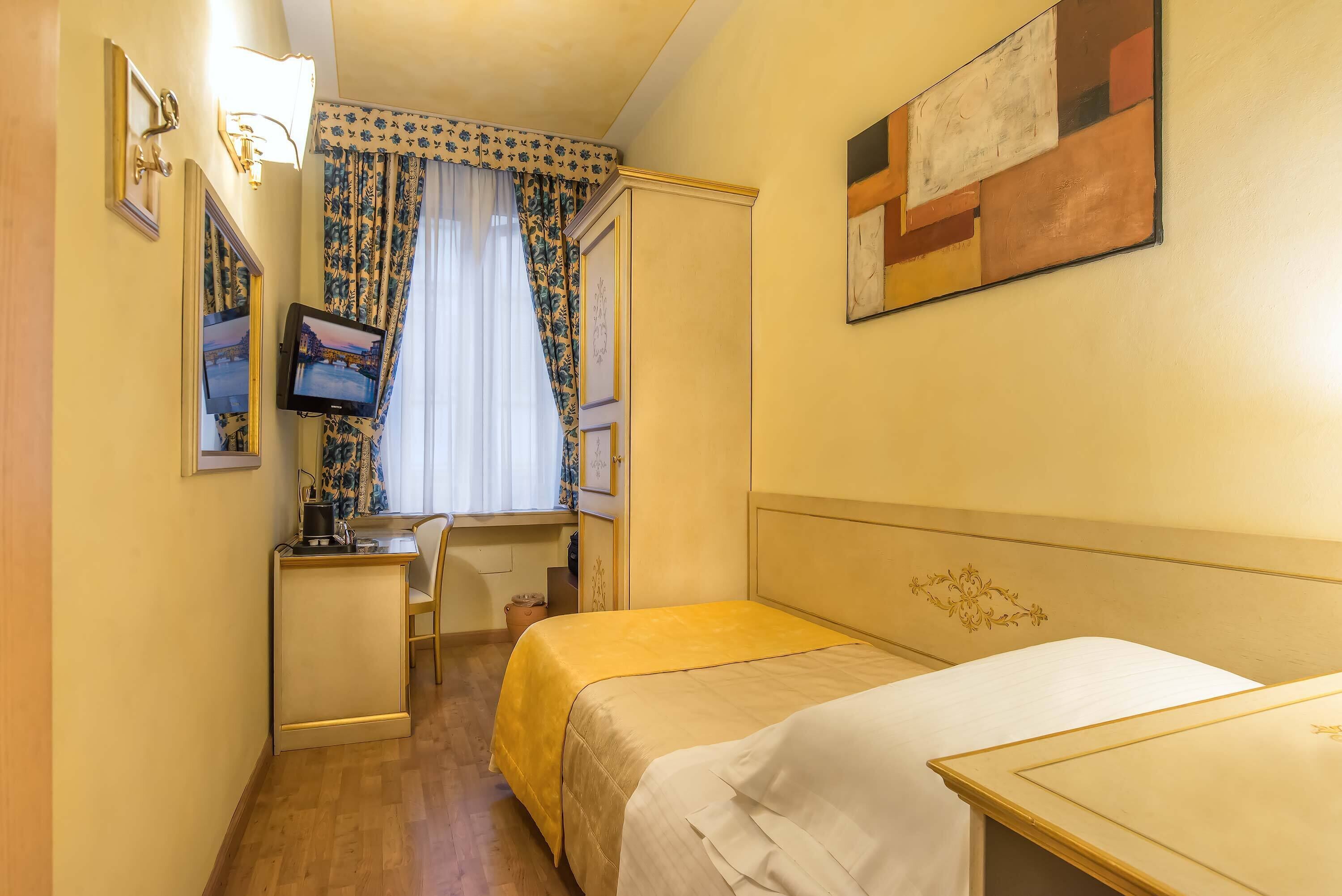 A hotel room with two beds, a desk, a chair, a television, and a window with curtains.