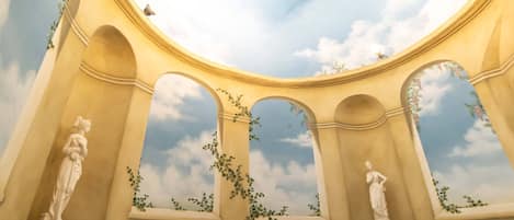 A room with a circular skylight, arches, and statues.