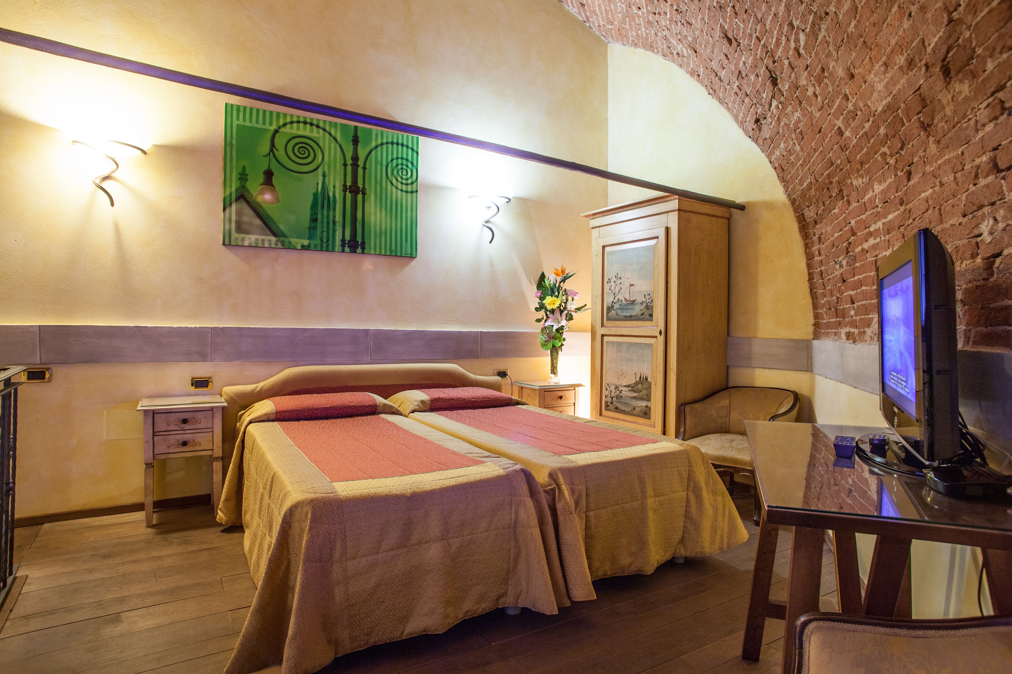 A hotel room with two beds, a TV, a desk, and a brick wall.