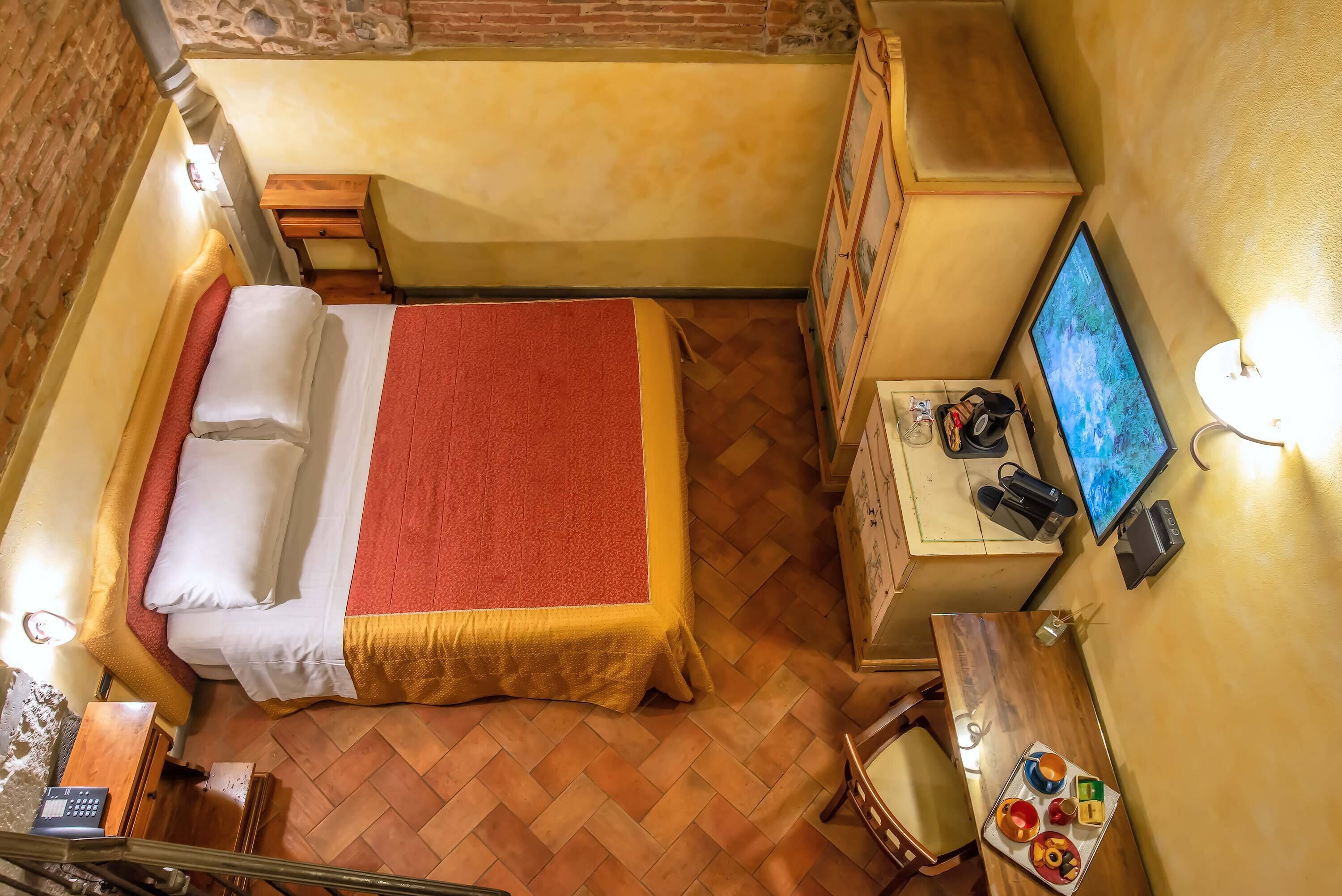 A small, cozy room with a bed, a desk, a chair, a television, and a small table with food.