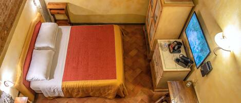 A small, cozy room with a bed, a desk, a chair, a television, and a small table with food.