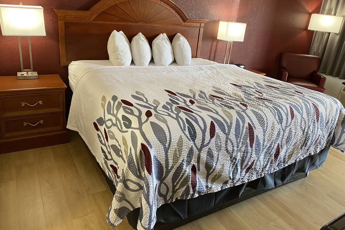 Ein Hotelzimmer mit einem hölzernen Kopfende, einem großen Bett mit weißen Kissen, einer gemusterten Decke und zwei Nachttischlampen.