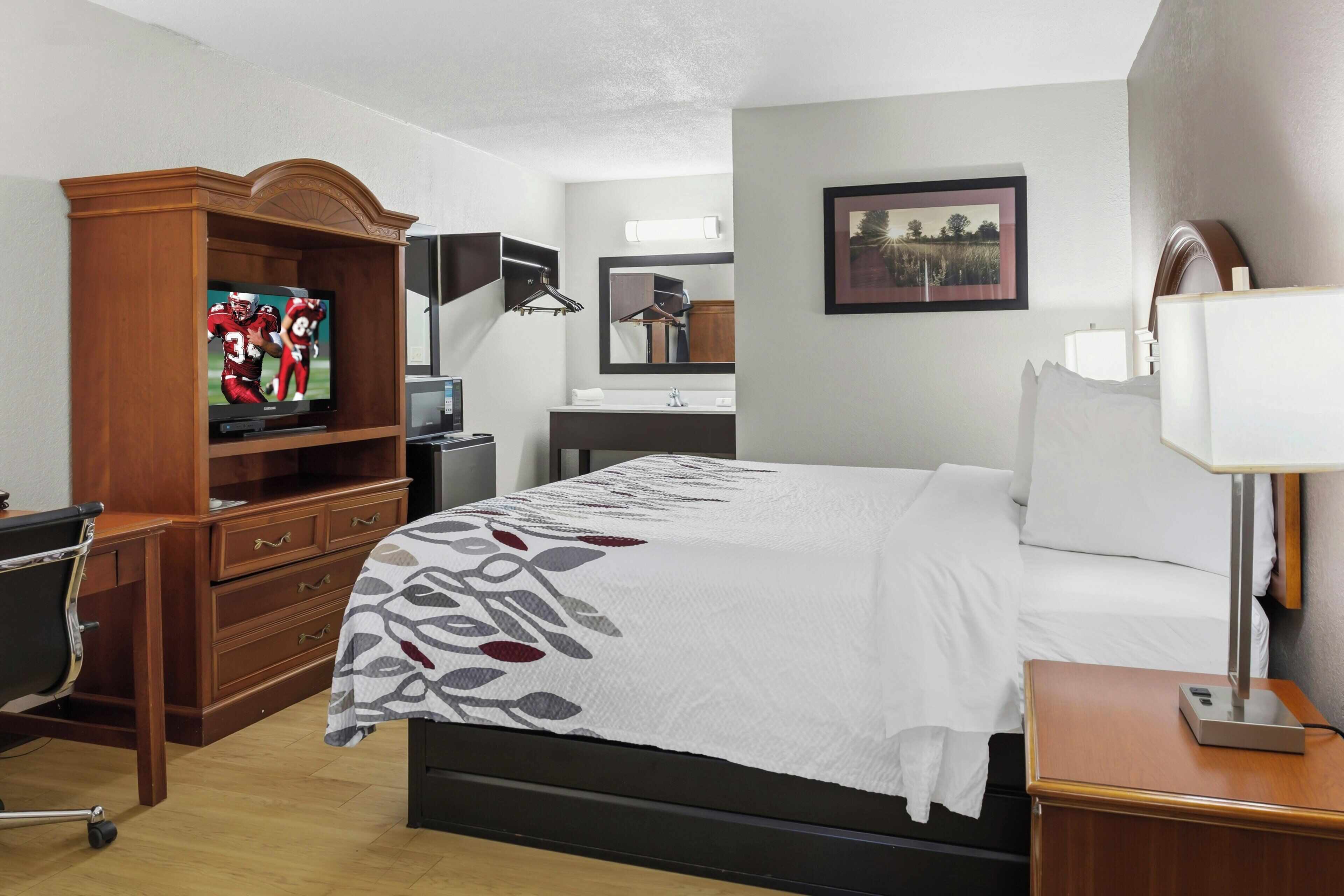 Habitación de hotel con cama, escritorio, televisor, cómoda, espejo y mesita de noche.