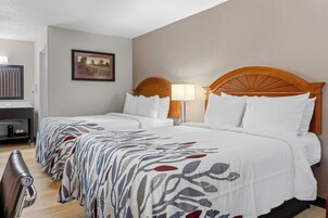 Habitación de hotel con dos camas, un escritorio, una silla, una lámpara y un cuadro en la pared.