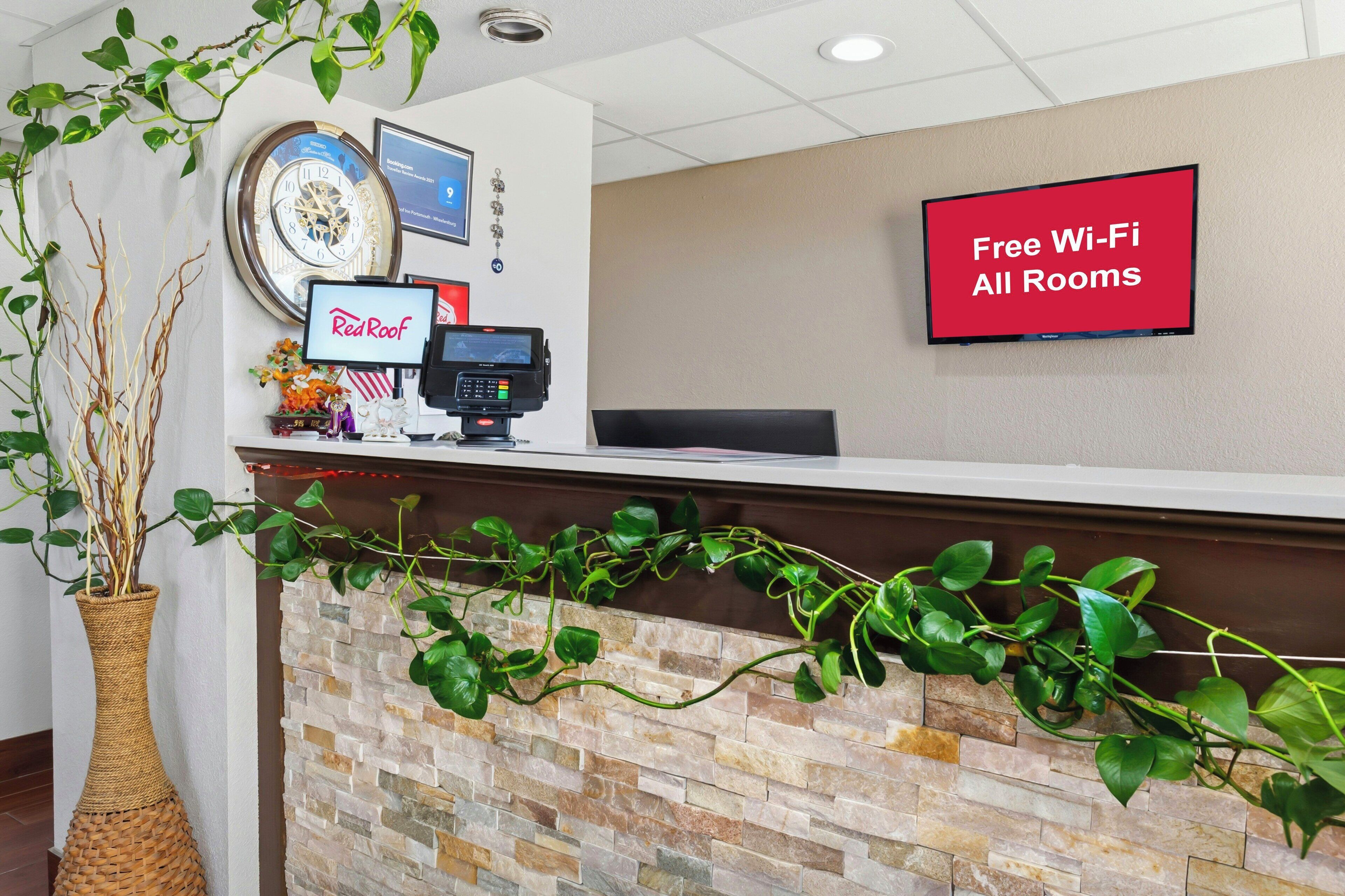 A reception area with a clock, a Red Roof sign, a Red Bull sign, a RedEye sign, and a TV displaying 'Free Wi-Fi All Rooms'.